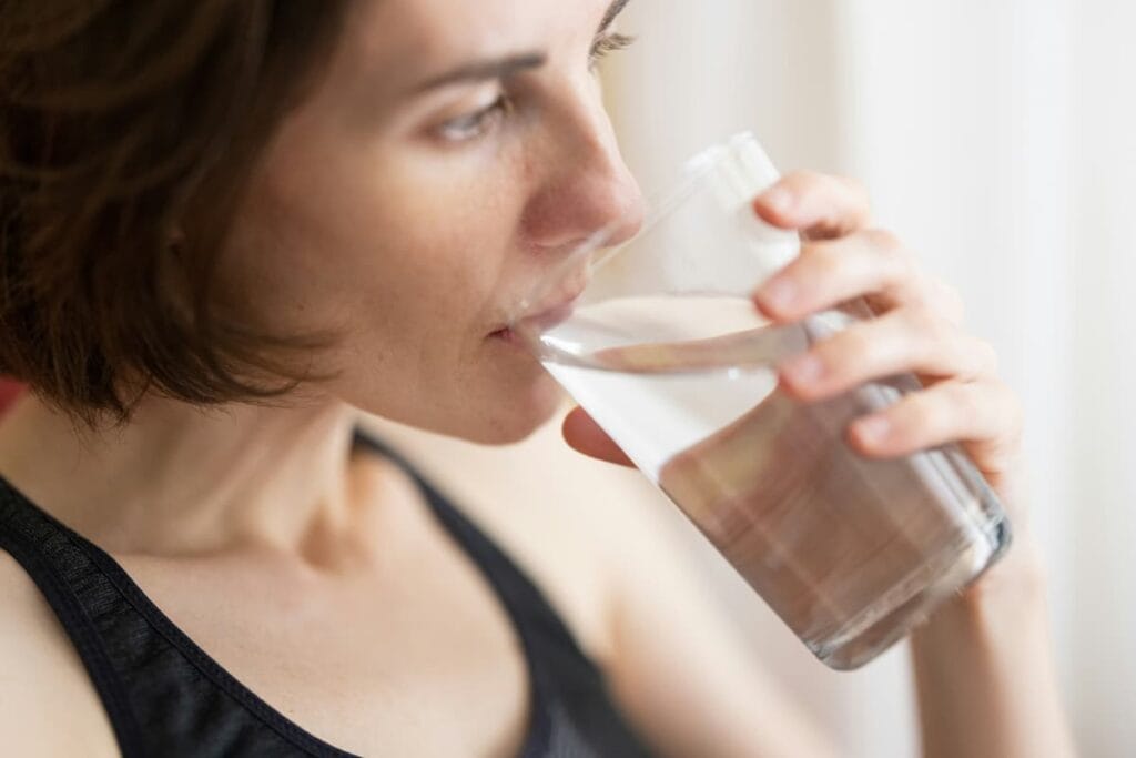 Woman drinking a glass of water with lemon, healthy habit to support digestion