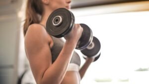 Woman lifting dumbbells in a bright gym, doing strength training to protect bone health